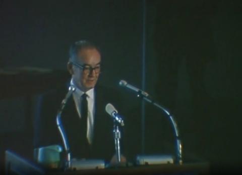 Still from 1967 video showing Walter Orr Roberts at a podium with microphones.