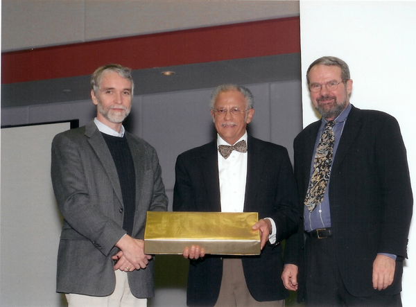 Tim Killeen, Warren Washington, and Rick Anthes pose together. Warren holds a gift.