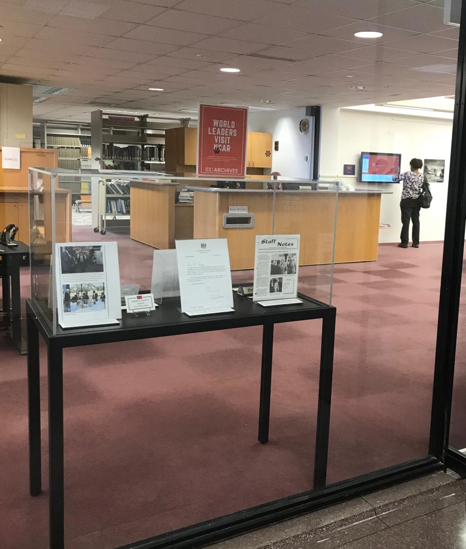 Exhibit display case as seen through the window into the Mesa Lab library. The case contains articles, photos, and nameplates related to world leaders who visited NCAR.