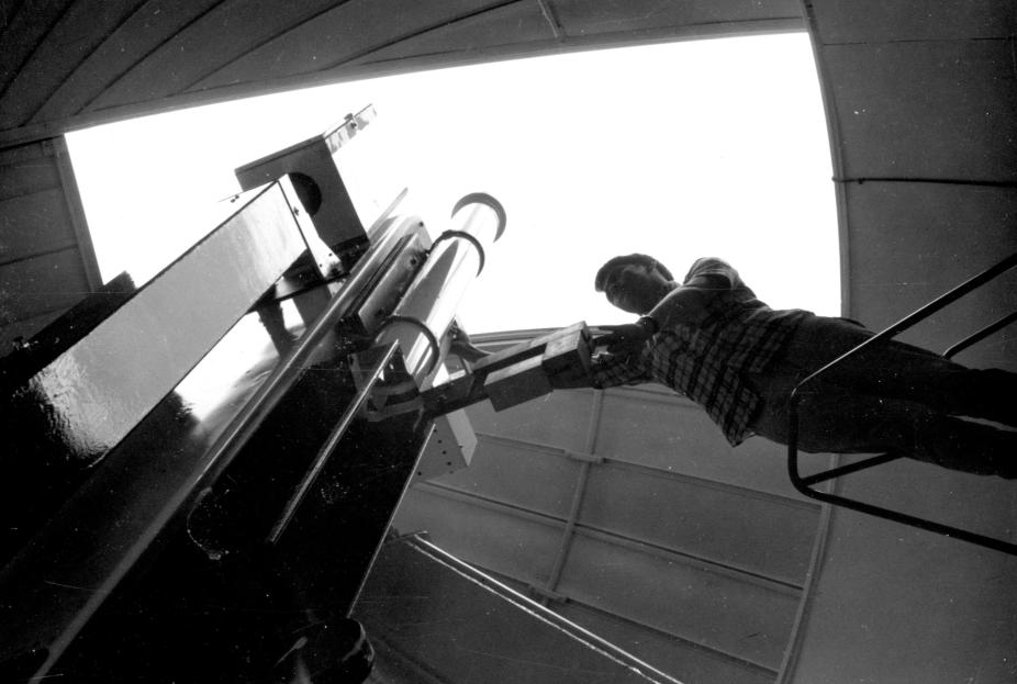 Photo taken from inside the observatory dome looking up at someone adjusting the equipment with the dome opening and the sky in the background