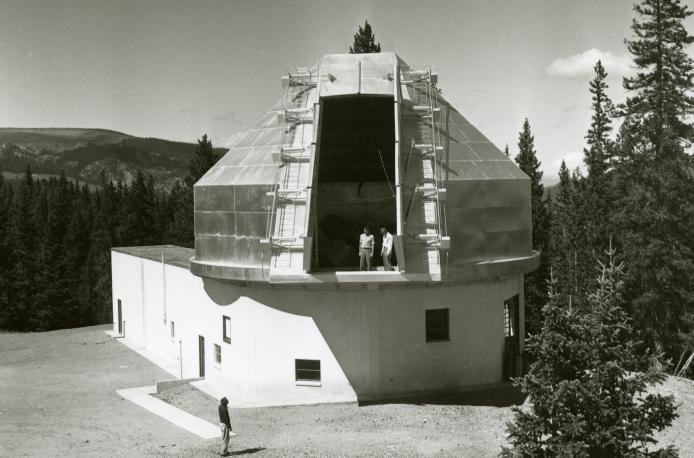 Climax observatory dome. There are a couple of people standing in the dome opening and another person below on the ground.