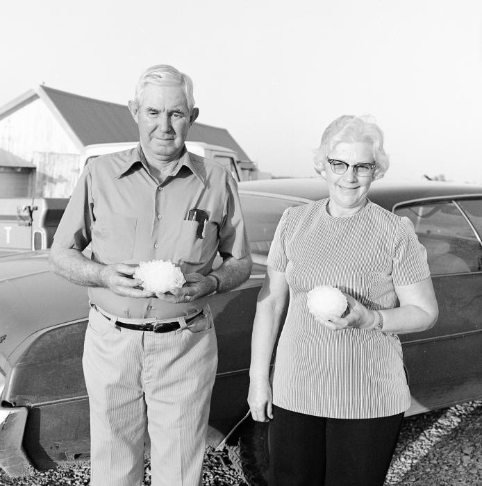 Man and woman posing together in front of a car. Each is holding a large hailstone.