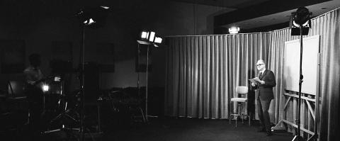 Photograph of Walter Orr Roberts as he stands in front of camera and lights for a video production.