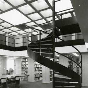 Spiral staircase in the Mesa Lab library. The staircase is surrounded by book stacks and there are skylights in the ceiling above.