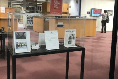 Exhibit display case as seen through the window into the Mesa Lab library. The case contains articles, photos, and nameplates related to world leaders who visited NCAR.